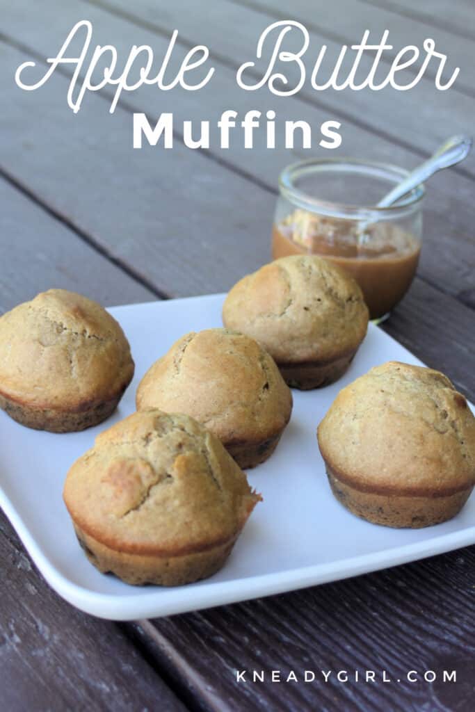 Apple butter muffins on a white plate sitting in front of an open jar of apple butter with a spoon sitting inside with text overlay.