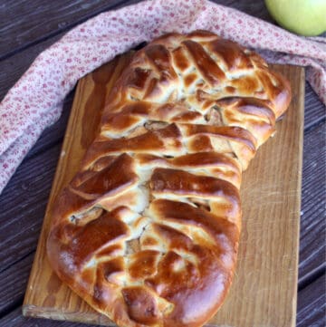 An apple cream cheese braid on a wooden cutting board with a napkin behind it and a green apple.
