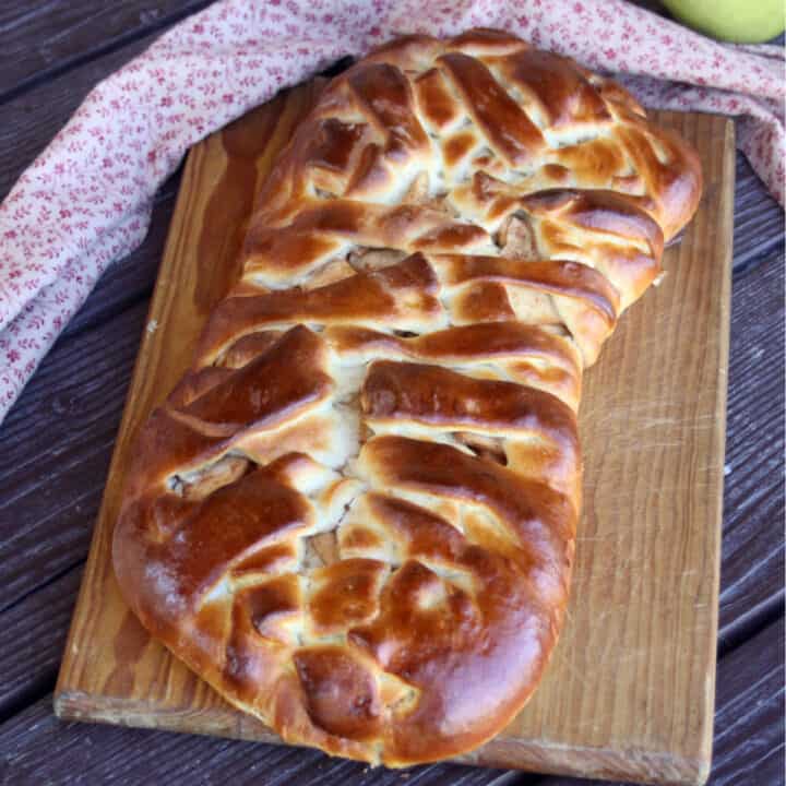 An apple cream cheese braid on a wooden cutting board with a napkin behind it and a green apple.