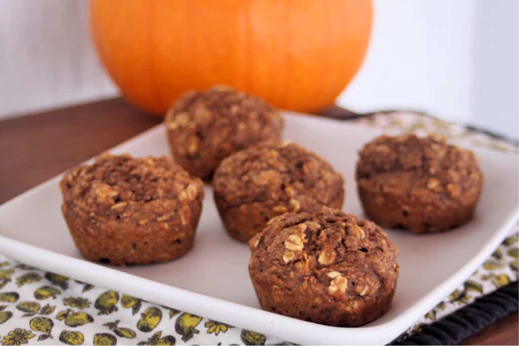 Healthy pumpkin muffins on a square white plate with a pumpkin in the background