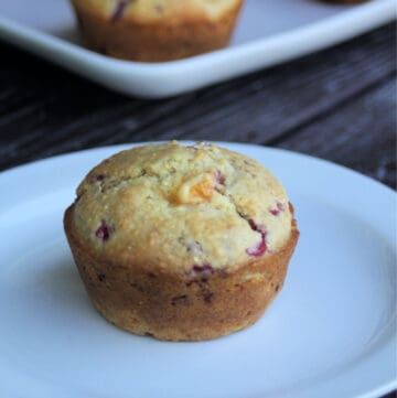 A peach raspberry cornmeal muffin on a white plate in front of another plate full of muffins.