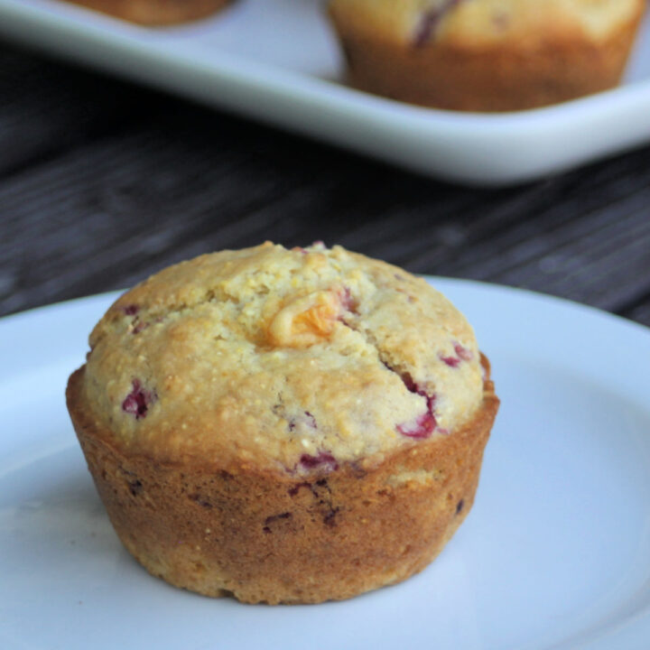 A peach raspberry cornmeal muffin on a white plate.