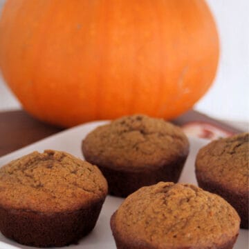 Pumpkin gingerbread muffins on a white plate with a pumpkin in the background.