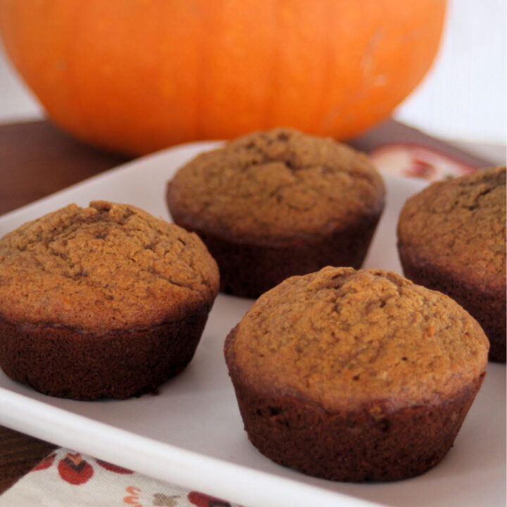 Pumpkin gingerbread muffins on a white plate with a pumpkin in the background.