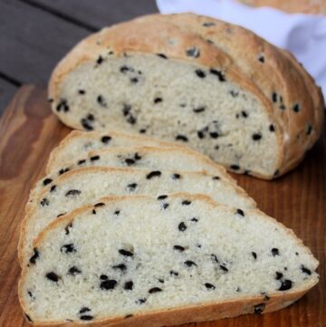 Slices of black olive bread on a board with remaining loaf in background.
