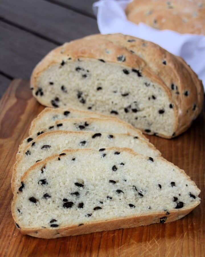 Slices of black olive bread on a board with remaining loaf in background.
