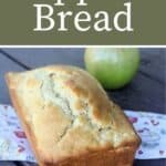 A loaf of apple bread sitting on a linen with green apple in the background and text overlay reading apple bread.