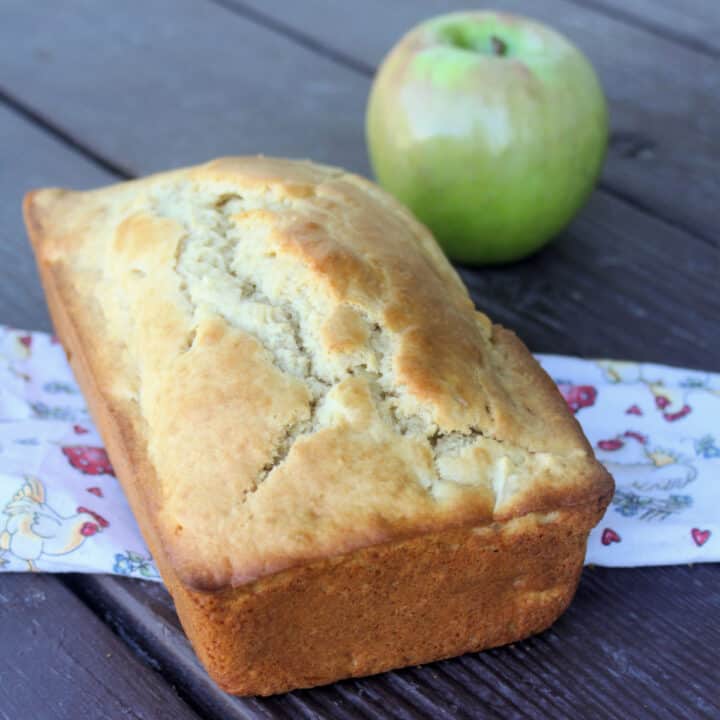 A loaf of apple bread sitting on a linen with green apple in the background.