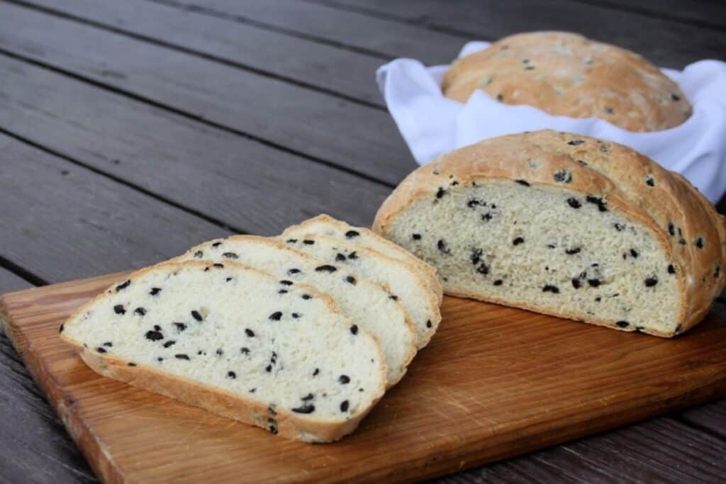 Slices of black olive bread on a board with remaining loaf in background.