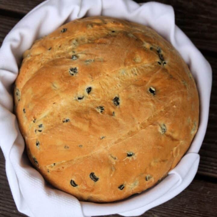 round loaf of olive bread in a napkin lined basket as seen from above.