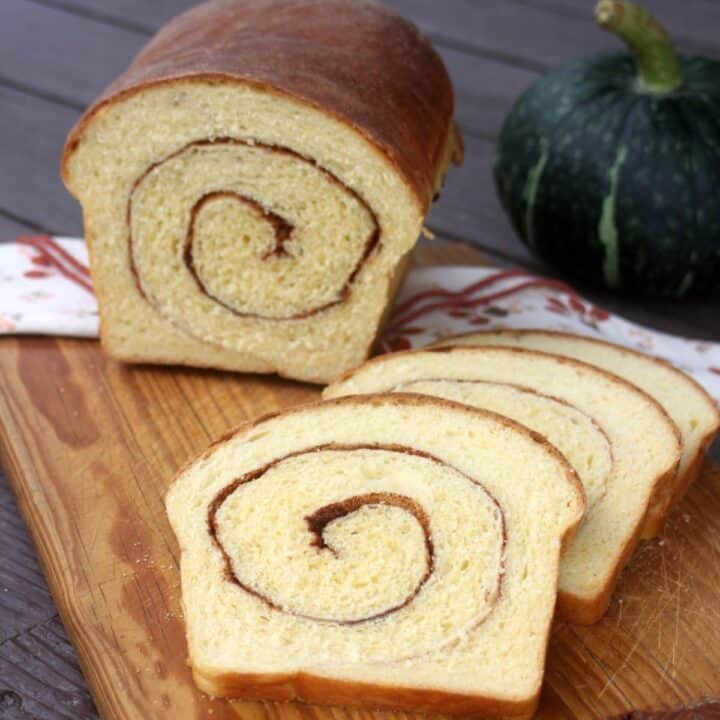 Slices of pumpkin cinnamon swirl bread on a cutting board with remaining loaf behind them and a green pumpkin in the background.