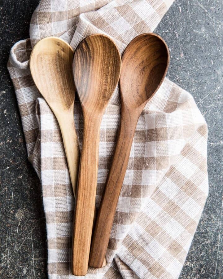 3 wooden spoons sitting on top of a brown and white plaid towel.