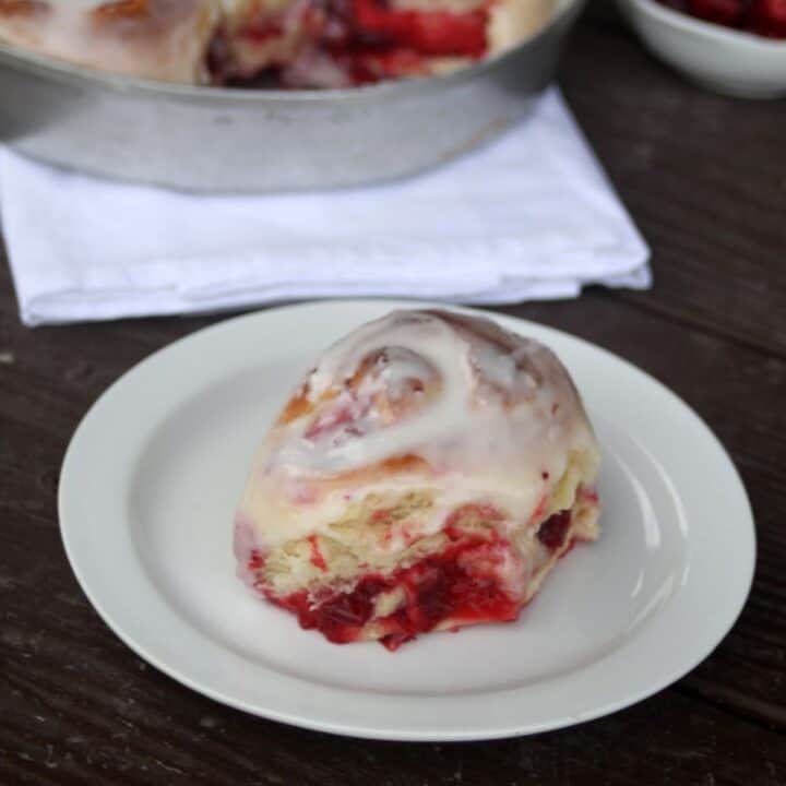 A frosted cranberry sweet roll on a white plate.