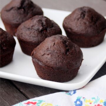 Chocolate muffins on a platter sitting behind a floral napkin.