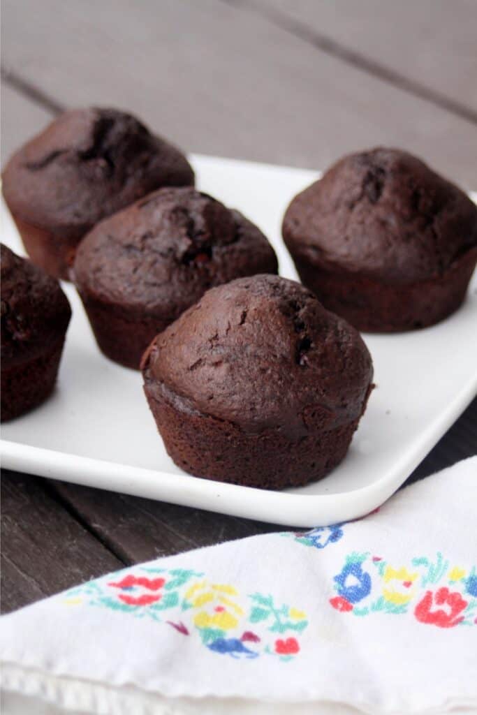 A platter full of chocolate muffins sitting behind a floral napkin.