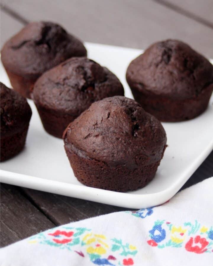 Chocolate muffins on a platter sitting behind a floral napkin.