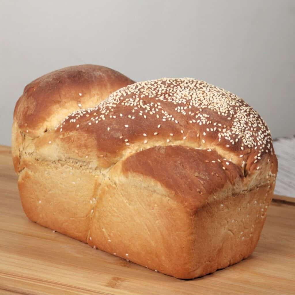 A loaf of bread with sesame seeds on the top sitting on a cutting board.