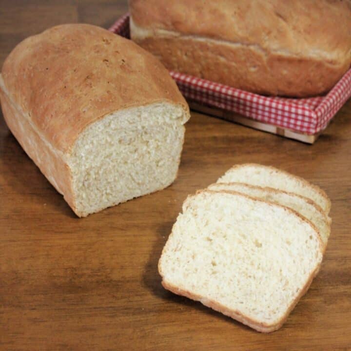 Slices of cream bread on a table sitting in front of the rest of the loaf with another loaf in a basket in the background.