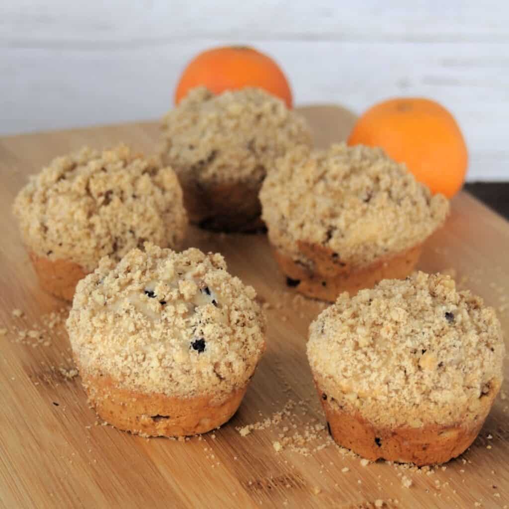 5 cranberry orange muffins on a wooden board with oranges in the background.