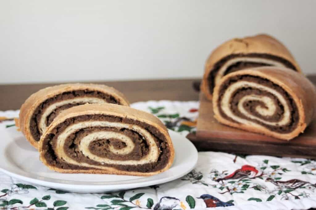 Slices of potica on a white plate sitting on top of a floral table runner with remaining loaf in the background.