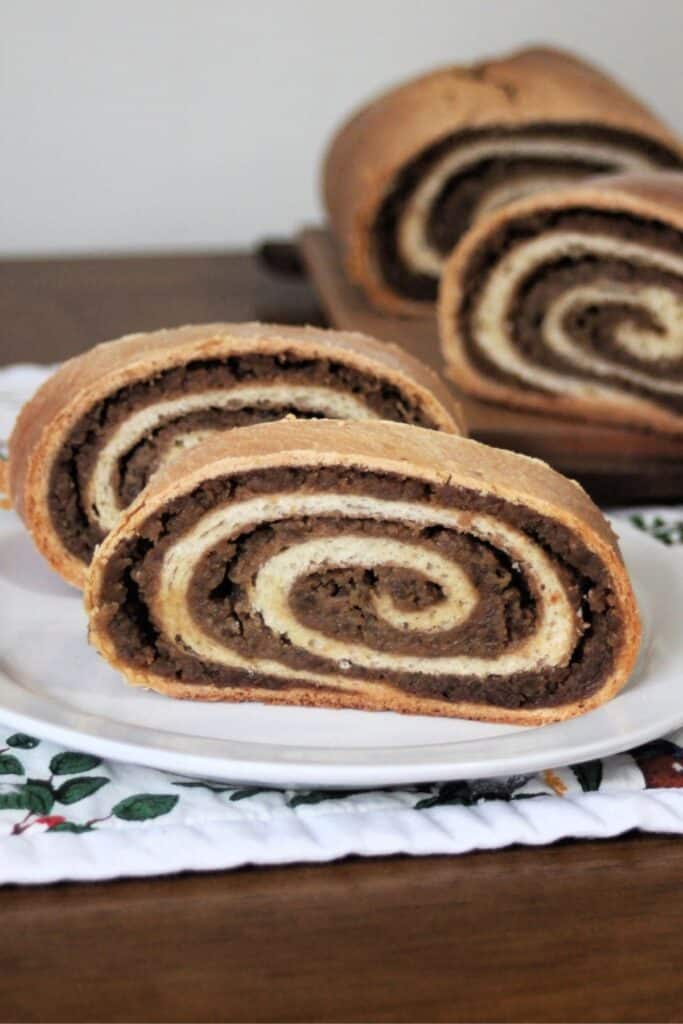 Slices of potica on a white plate sitting on top of a floral table runner with remaining loaf in the background.