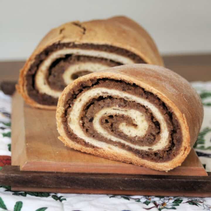 A loaf of potica sliced in half with insides exposed sitting on a wooden cutting board.