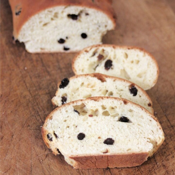 Slice of rum raisin bread on a cutting board with remaining loaf in background.