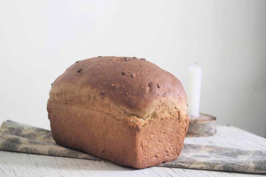 A loaf of sunflower seed bread sitting on a napkin in front of a taper candle in a holder.