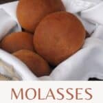Molasses brown bread rolls stacked in a white napkin lined basket with text overlay stating molasses dinner rolls.
