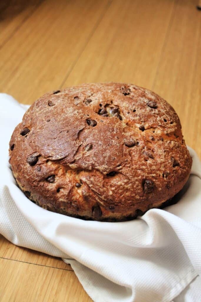 A round loaf of chocolate chip bread in a white linen lined basket.