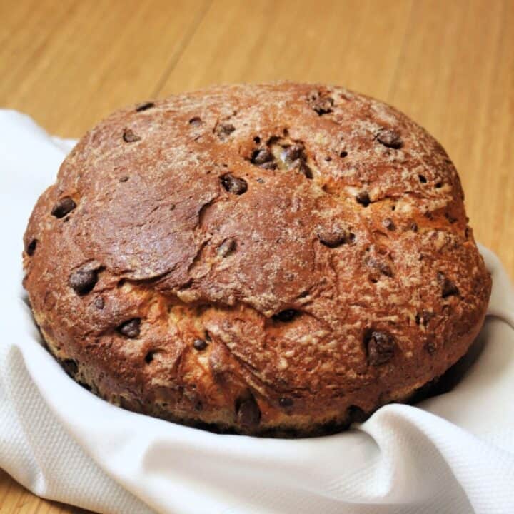 A round loaf of chocolate chip bread in a white linen lined basket.