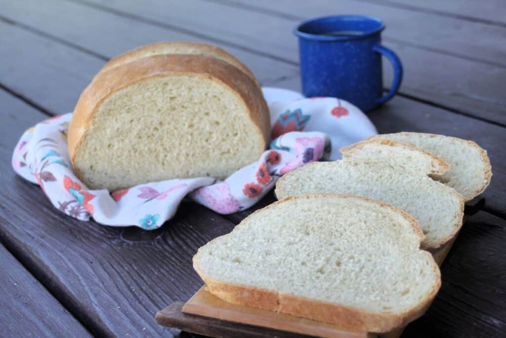 Slices of coffee bread staggered on a board with the remaining loaf sitting on a floral cloth slightly behind it and a blue tin cup of black coffee.