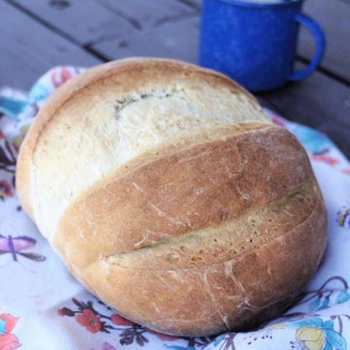 A round loaf of coffee bread on a floral cloth with a blue coffee cup in the background.