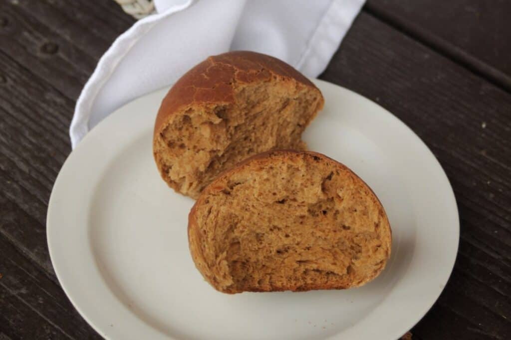 A molasses brown roll split in half sitting on a plate with a white napkin.