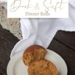 A molasses roll split in half on a white plate sitting in front of a basket of more rolls with text overlay stating: dark & soft dinner rolls.