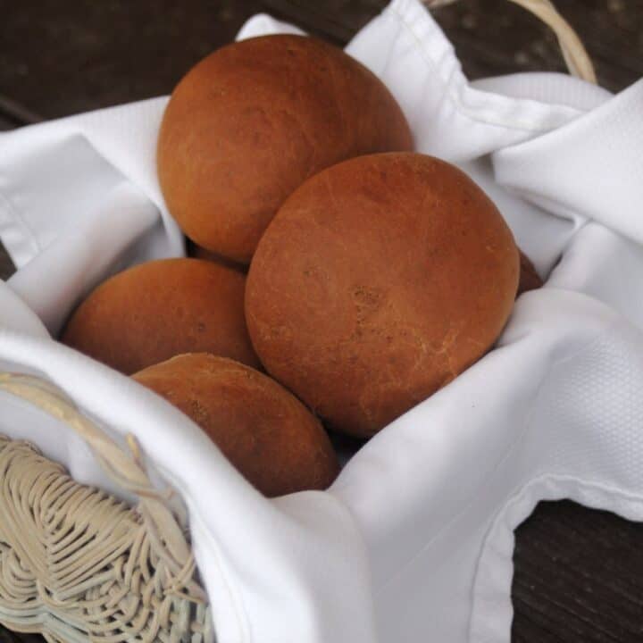 Dark molasses dinner rolls stacked in a white napkin lined basket.