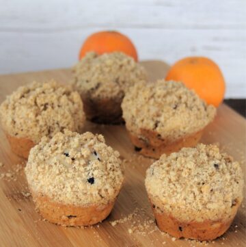 Dried cranberry muffins on a wooden board with fresh oranges in the background.