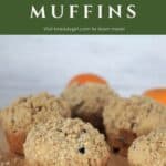 Muffins lined up on a board with oranges in the background and text overlay reading: Cranberry Orange Muffins.