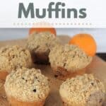 Muffins lined up on a board with oranges in the background and text overlay reading: Cranberry Muffins.