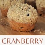A close up of a muffin on a board with other muffins in the background with text overlay stating: cranberry muffins.