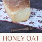 A loaf of honey oat bread on a brown and white napkin with a wooden honey dipper sitting in front of them with text overlay stating: honey oat bread.