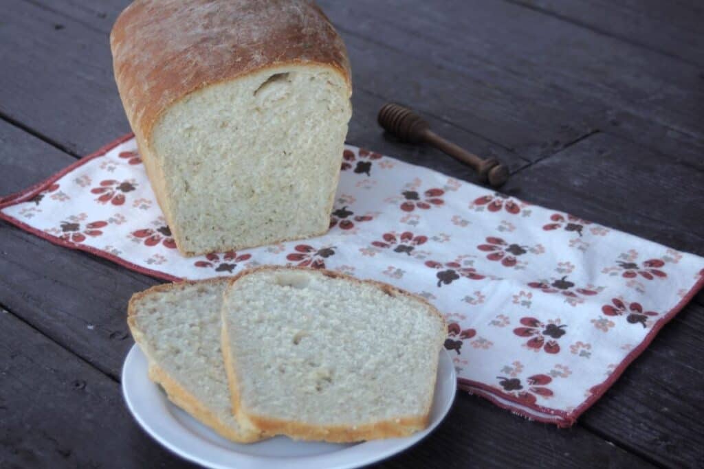 Slices of honey oat bread on a white plate sitting in front of the remaining loaf on a napkin.