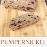 A slice of bread on a wooden cutting board with remaining loaf and red heart shaped container in the background with text overlay stating: pumpernickel raisin bread.