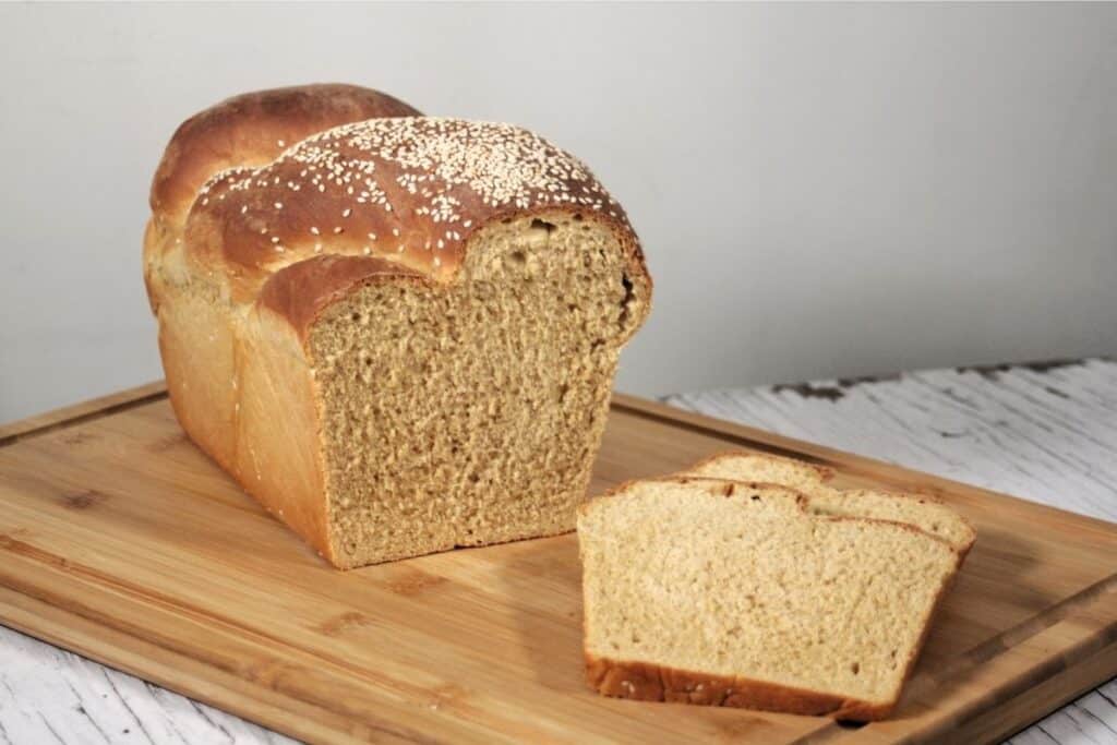 Slices of sesame bread sitting on a wooden cutting board with remaining loaf behind them.