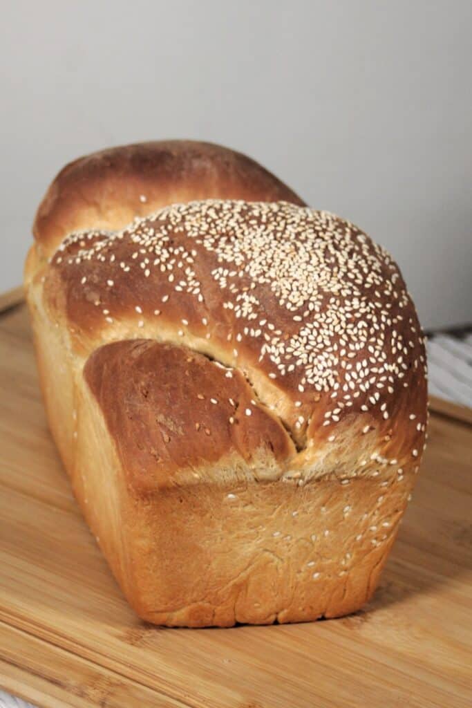 A loaf of sesame bread on a wooden cutting board.