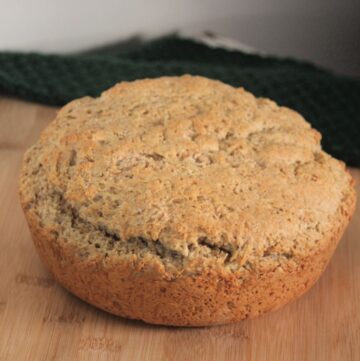 A round loaf of irish oatmeal soda bread sitting on wooden board with green cloth in background.
