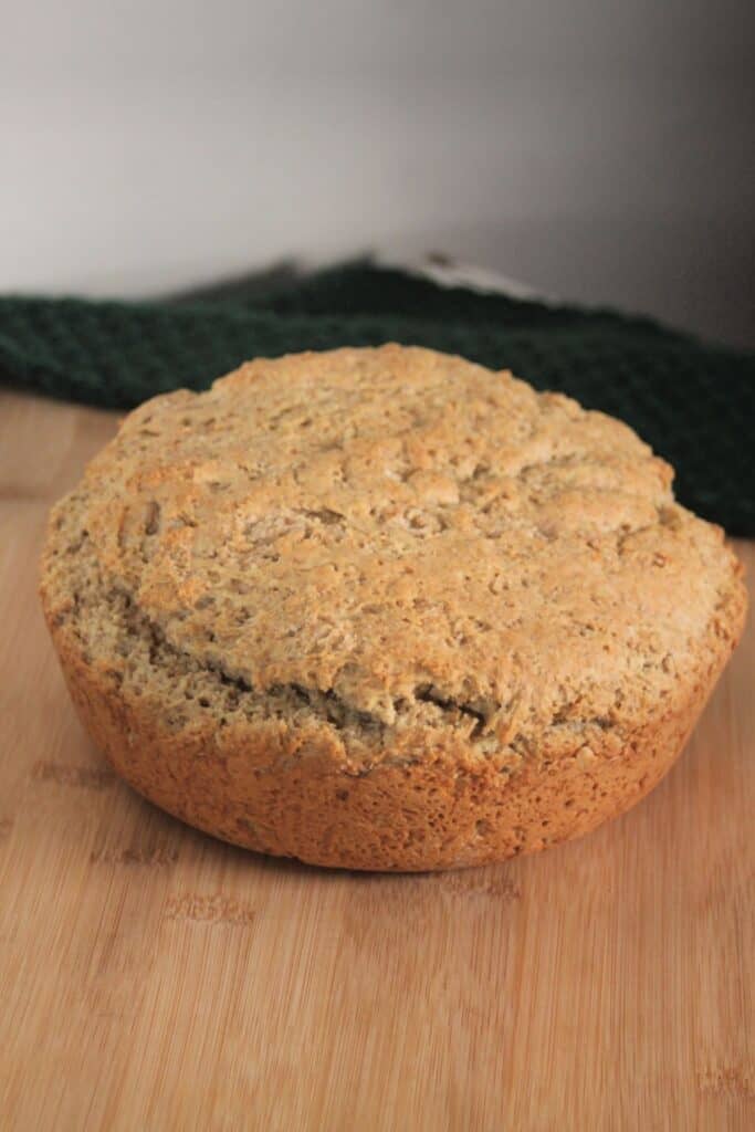 A round loaf of irish oatmeal soda bread sitting on wooden board with green cloth in background.