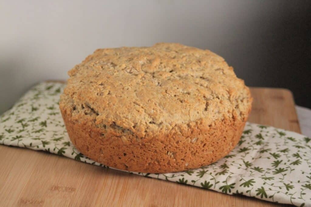 A round loaf of irish oatmeal soda bread sitting on a green and white table linen.
