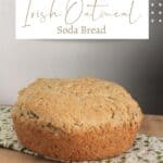 A round loaf of irish oatmeal soda bread sitting on a green and white table linen with text overlay stating Irish Oatmeal Soda Bread.