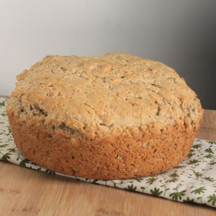 A round loaf of irish oatmeal soda bread sitting on a green and white table linen.